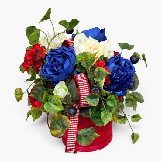 TCTCrafts patriotic floral arrangement in a red basket with red, white, and blue artificial flowers and greenery.