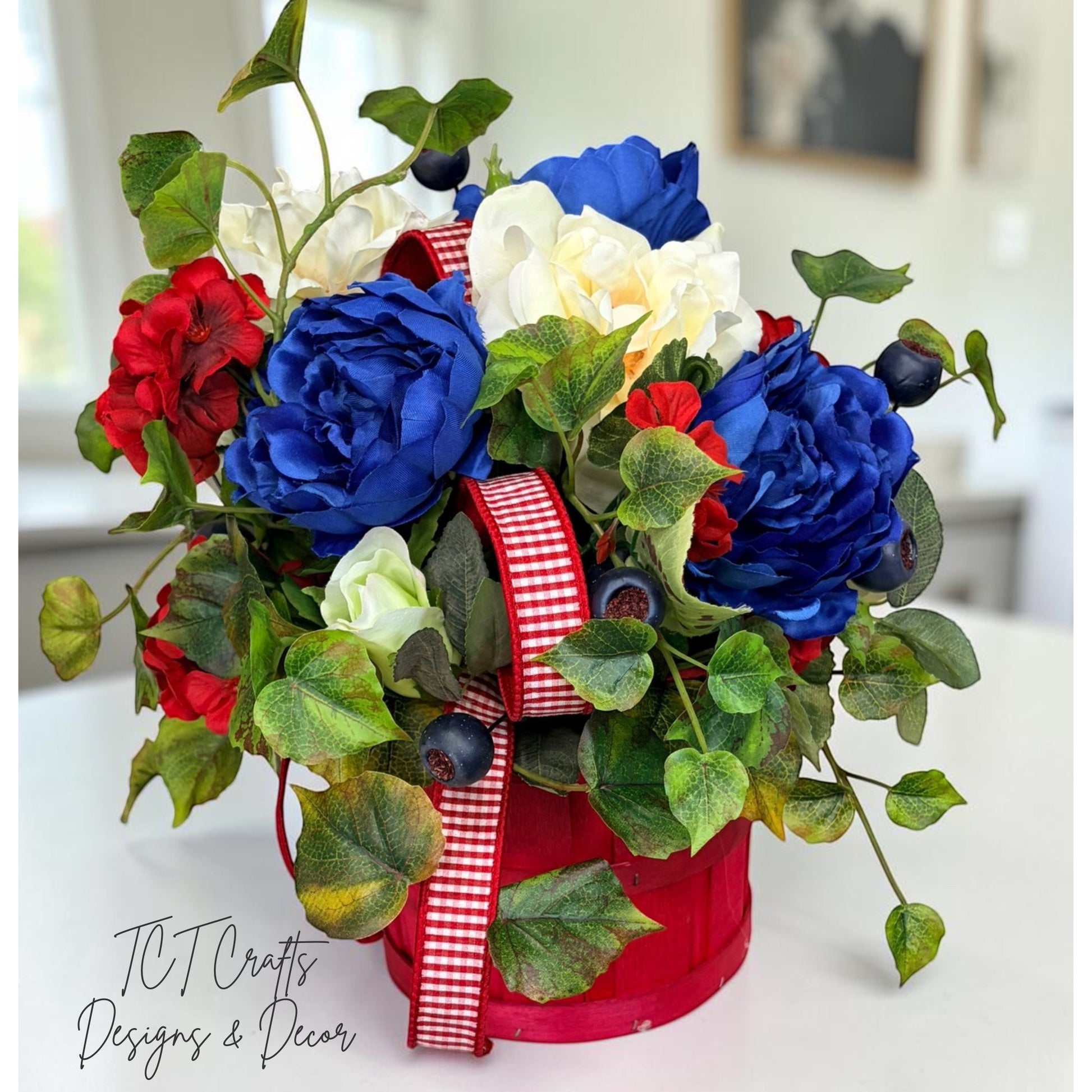TCTCrafts patriotic floral arrangement in a red basket with red, white, and blue artificial flowers, greenery, and ribbon.