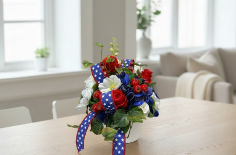 TCTCrafts patriotic floral arrangement with red roses, blue hydrangea, white cosmos, and greenery in a white container with star-spangled ribbon.